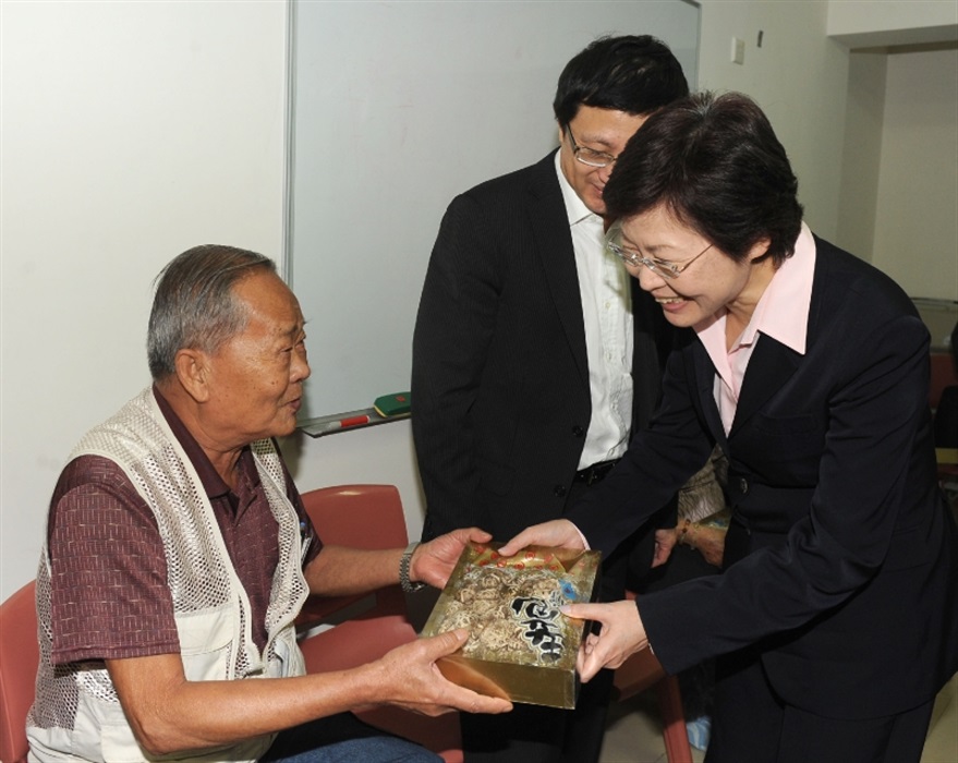 The Secretary for Development, Mrs Carrie Lam, presents a souvenier to an elderly man.